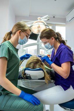 Kadın dişçi, asistanın yardımıyla hastanın ağız boşluğunu profesyonel bir muayeneden geçirir..