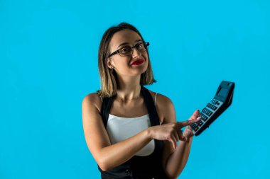 Mavi arka planda izole edilmiş hesap makinesi tutan gözlüklü genç ve güzel bir iş kadını. Kariyer başarısı zenginlik .iş muhasebe kavramı.