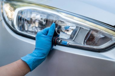 Bir arabanın nasıl tamir edileceğini bilen bir adam araba tamiri için ampulleri tutar. Arabadaki farların yerine farlar.