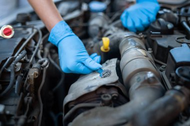 Erkek tamirci, kadının araba arızası sorununu çözmesine yardım ediyor. Hasarlı parçayı onarmak için arabanın kaputunu kaldırır. Adamın elleri kapalı.