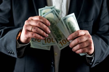 Gömlekli ve ceketli bir işadamı göğsünün önünde yüz dolarlık banknotlar sayıyor. Para ve ticaret kavramı. Yakından.