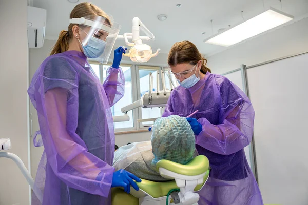 dentists with mirror, drill and dental air water gun spray treating adult patient teeth at dental clinic