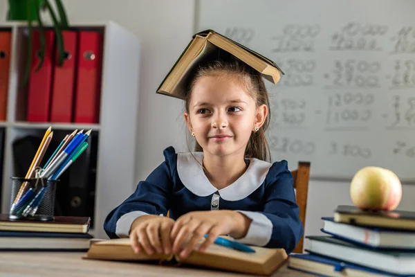 cute industrious child is sitting at a table indoors. The child is studying in the classroom on the background of the blackboard. The girl is reading a book. Back to school and happy times
