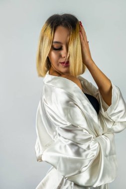 İpek beyaz bornozlu güzel sarışın kız. Güzel bir arka planda izole edilmiş. ev kıyafetleri
