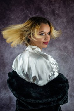 Üstü kalın siyah kürklü, güzel, açık ipek bornozlu genç bir kadın başını çeviriyor. dumanlı arka planda izole edilmiş. konsept kadın portresi