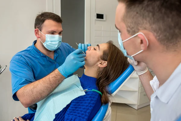 Dentist and assistant in masks and uniforms making professional teeth cleaning female patient at dental office. stomatology healthcare