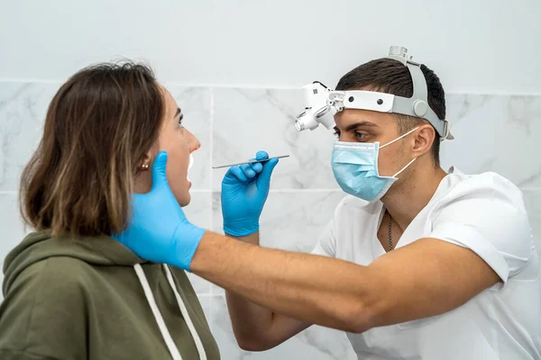 doctor using an inspection spatula to examine a patient\'s throat. An ENT doctor examines a woman\'s throat. the patient opened his mouth to examine the throat