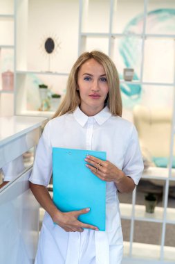 Kasanın yanındaki hastane koridorunda beyaz üniformalı genç bir hemşire poz veriyor. Hemşire konsepti. tıbbi uzmanlar.