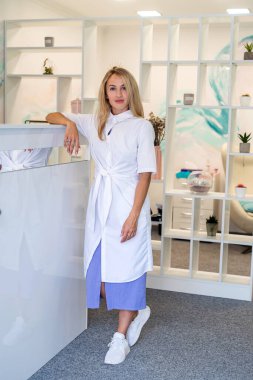 Kasanın yanındaki hastane koridorunda beyaz üniformalı genç bir hemşire poz veriyor. Hemşire konsepti. tıbbi uzmanlar.