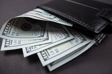 Tahta bir masanın üzerinde para dolu deri cüzdan ve üzerinde Başkan Franklin 'in portresi olan yüz tane Amerikan banknotu. 100 dolarlık nakit para. kağıt para birimi arkaplanı.