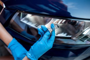 Eldivendeki güçlü el bir arabanın arka farı üzerinde iki gelagon lambası tutuyor. Araba tamiri konsepti. Profesyonel bir oto tamircisi