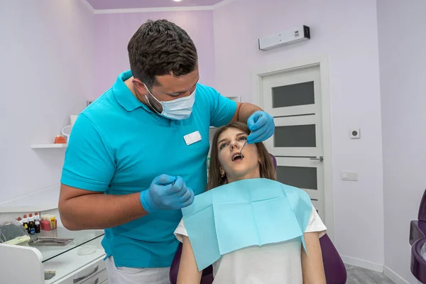 male dentist examines the teeth of a young patient in the office. The concept of doing dentist