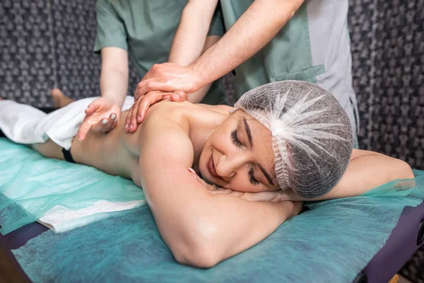 Back massage in four hands at the same time - two professional massage therapists deal with a female patient. spa salon. skin healing. muscle tone