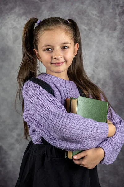 cute little girl is holding a book or books on a plain wall background in a studio. The concept of a girl with books. isolated teaching