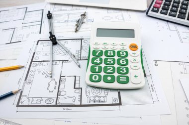 Bina planları kask ve çizim aletleriyle çiziliyor. Çizimler üzerindeki inşaat araçları