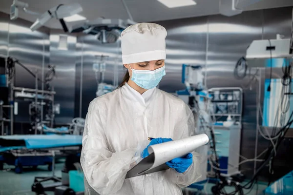 female doctor standing in an operating room in a modern clinic is writing on a clipboard with information for a patient. concepts of medicine. people\'s health operating room