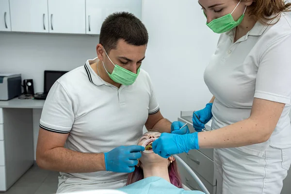 Mandlig Tandlæge Udfører Behandling Med Assistent Til Tilfreds Kvindelig Klient - Stock-foto