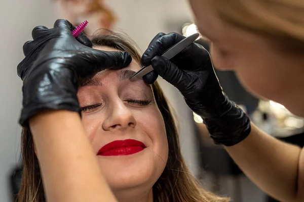 Close-up of a young woman during an eyebrow correction procedure in a beauty salon. tweezers. eyebrow epilation