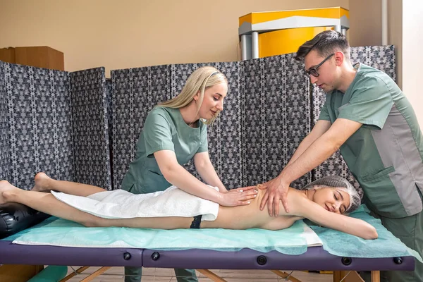 Massage in four hands over the patient's back is performed by two massage therapists, a woman and a man, at the same time. effective therapeutic massage. spa salon healthy body