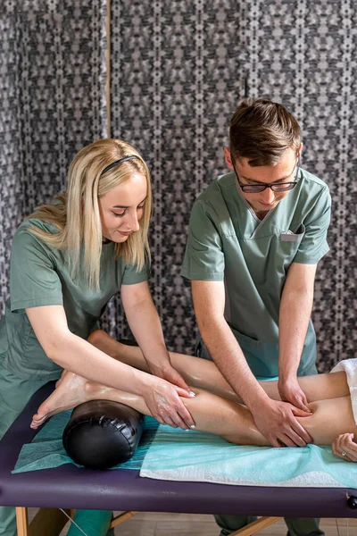 Two massage therapists, a woman and a man, give a double foot and leg massage to a girl in a spa salon. Four hands of masseur during massage close up. spa salon