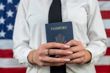 cropped portrait of a young flight attendant holding a fan of dollars and an American passport and standing against an American flag background. travel passport control