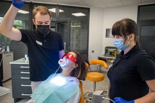 dentist with an assistant in overalls uses UV lamps, then treats the patients\' teeth. The concept of tooth restoration