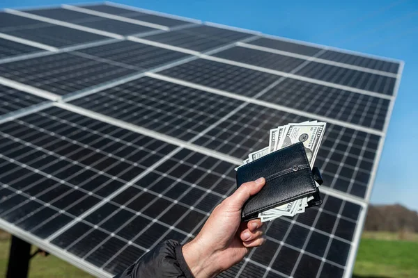 Female hand with dollars in a black wallet on the background of solar panels. Solar energy business. the cost of green electricity. New technologies. the energy of the future