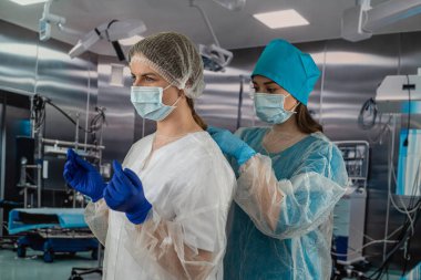 Tıbbi maskeli iki kadın doktor ameliyathanede yardım almaya hazırlanıyor. İlaç. İki hemşire. Doktorların portresi