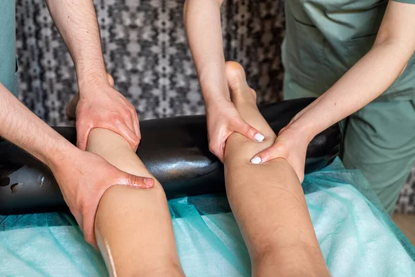Two massage therapists a woman and a ma give a double foot and leg massage to a girl in a spa salon. Four hands of masseur during massage close up