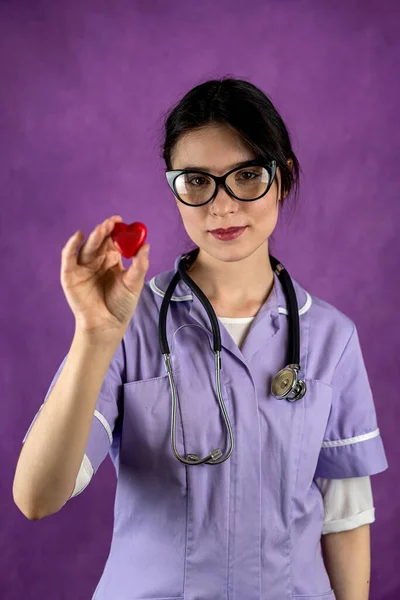 Young female doctor in hospital clothes mask and gloves holding a small red heart as a symbol in the hospital. Operational. Nurse. Heart symbol
