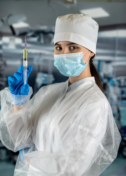 Portrait of a female doctor in a face mask wearing gloves prepares a syringe with medicine in the operating room. Healthcare concept. Preparation for surgery. patient\'s health