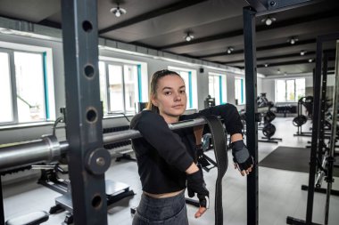 Kız, fazladan kilo vermek için geniş bir spor salonunda yeni bir simülatörle güç egzersizleri yapıyor. Doğal ışıklandırma.