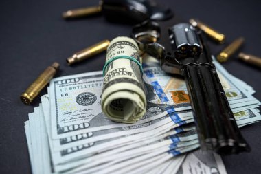 Silah ve mermi kovanları siyah arka planda Amerikan dolarlarının yanında. Suç ve hukuk kavramı. Suçlu parası ve cezası.