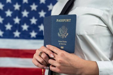 cropped portrait of a young flight attendant holding a fan of dollars and an American passport and standing against an American flag background. travel passport control
