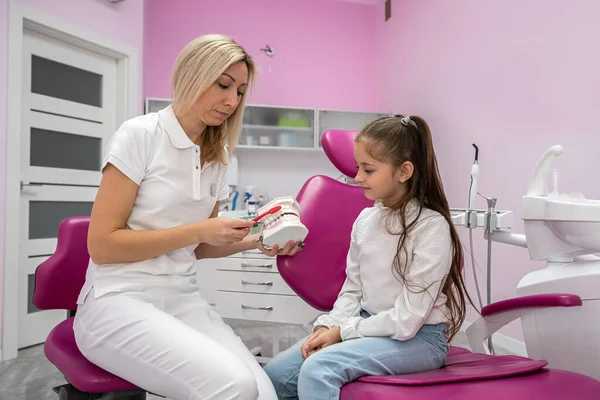 small patient sits in the dentist\'s chair where the dentist tells her how to brush her teeth correctly. the concept of treatment of children\'s teeth.