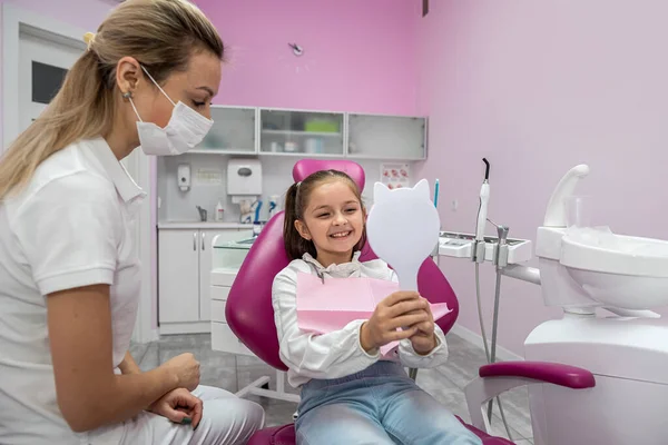 little female patient in the dental chair looks at her teeth after their treatment. dental office. mirror in hands