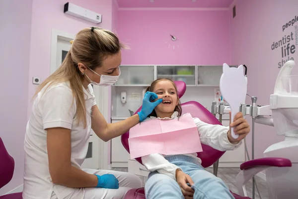little patient admires her healthy teeth in the reflected mirrors. dentistry examination of children's teeth