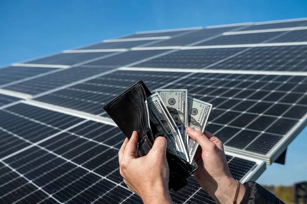 Money dollars in a wallet holding hands over a solar panel. Banknotes on the panel. Concept of cheap solar energy.