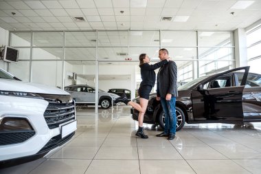 an extremely happy woman is happy when her husband bought a car at a car dealership. happy couple in salon. car purchase