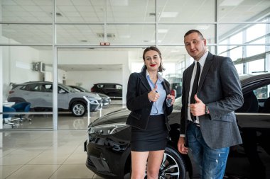 young couple buys a car at a car dealership and is sincerely happy about such a purchase. the concept of buying and selling a car. car dealership