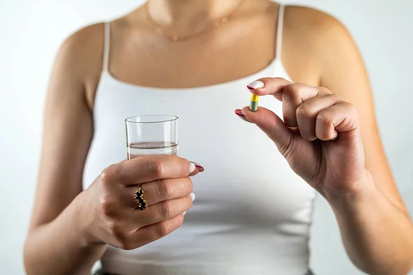 woman takes cosmetic supplements for glowing skin while holding fish oil capsules and a glass of water. isolated on white background. female hands capsule and water in a glass