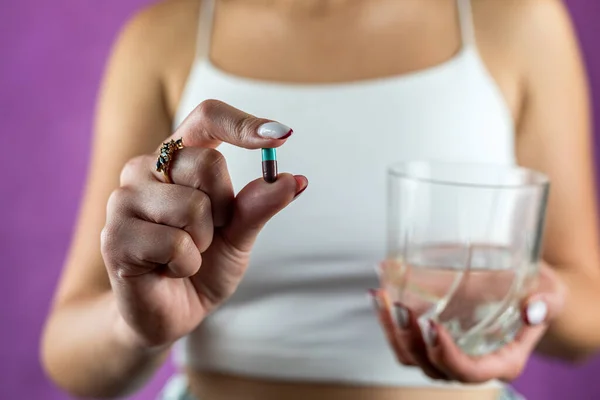 Female hands holding one weight loss pill and a glass of water close-up. fat burning weight loss