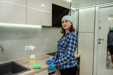 beautiful young girl cleans the kitchen wearing special gloves and special means that dissolve and remove grease from surfaces. The girl smiles while cleaning. the best cleaning products