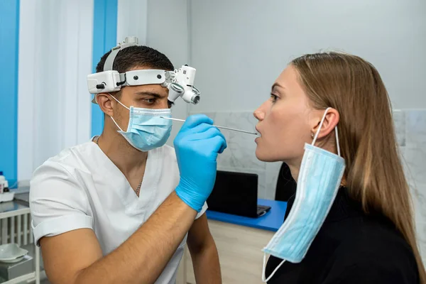 Doctor using an inspection spatula to examine the throat of a woman patient. An ENT doctor examines a woman\'s throat. the patient opened his mouth to examine the throat