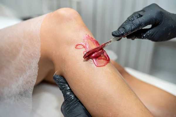 Master of depilation doing applying of sugar paste for the procedure of epilation hair removal on leg at spa studio.