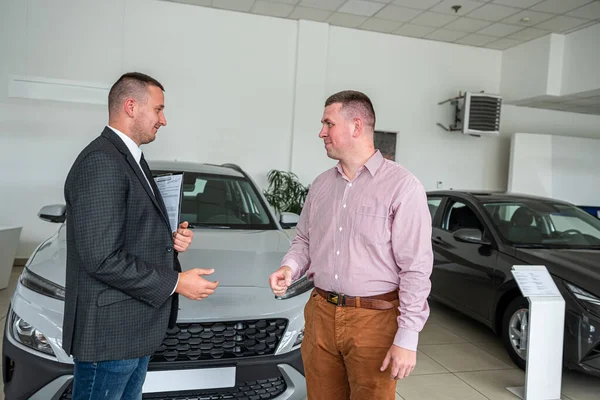 young male client choosing and buying car with help a professional sales agent at modern car showroom