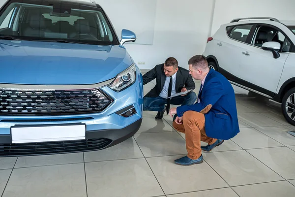 young male client choosing and buying car with help a professional sales agent at modern car showroom