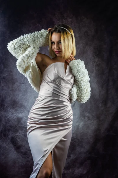 woman in a fur coat and a dress is photographed in a fashion studio isolated. of a beautiful sensual woman with white hair in a luxurious dress. portrait of a woman