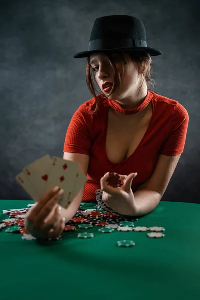 beautiful young girl in a red dress and with a hat on her head came to play poker. casino. poker. playing cards and chips