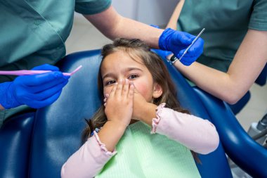 little girl closes her mouth with her hands on the doctor's dental chair. The concept of dental treatment in children